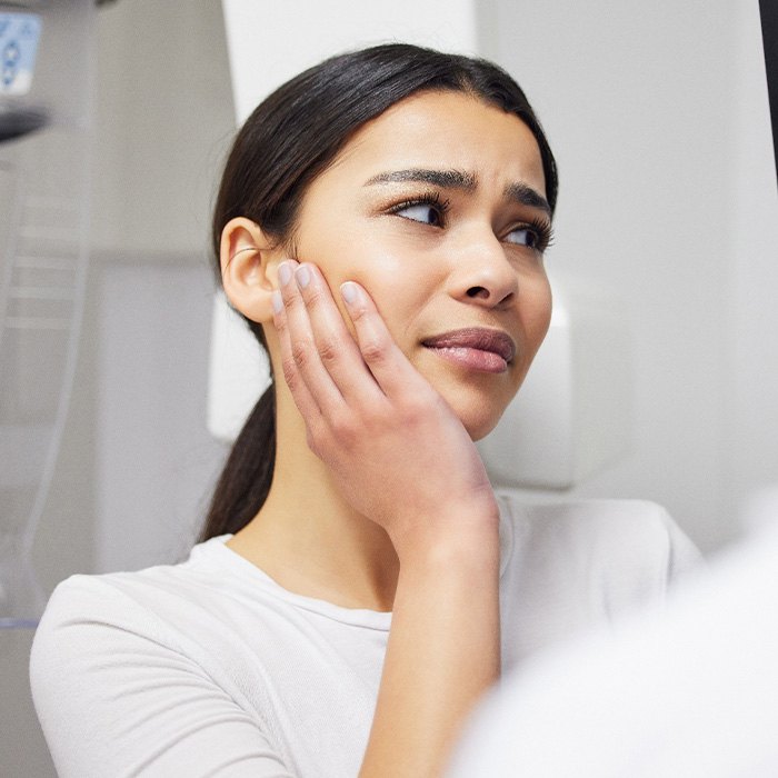 Woman in white shirt talking to dentist holding hand to jaw in pain