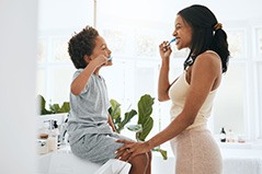 Woman and boy in the bathroom facing each other brushing teeth