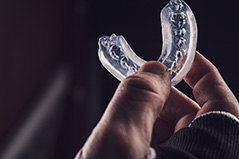 Thumb and pointer holding clear mouthguard with black background