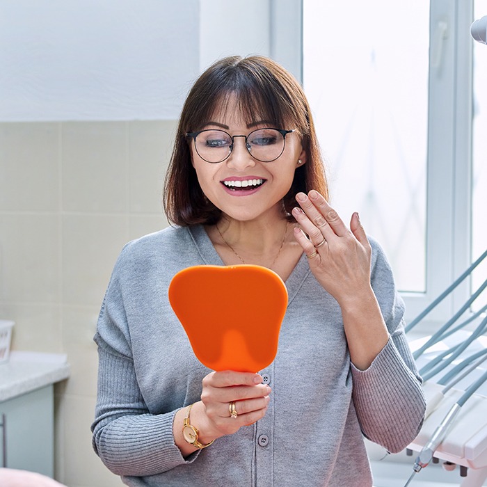 A happy female dental patient admiring her smile in a hand mirror