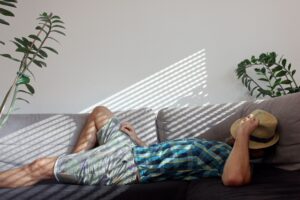 Man in checkered shirt with straw hat asleep on the couch in a sun beam